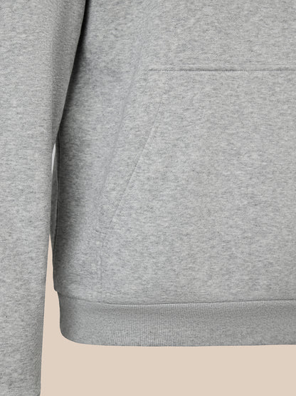 Close-up of a heather gray sweatshirt showing the chest pocket, sleeve, and ribbed hem against a light beige background.
