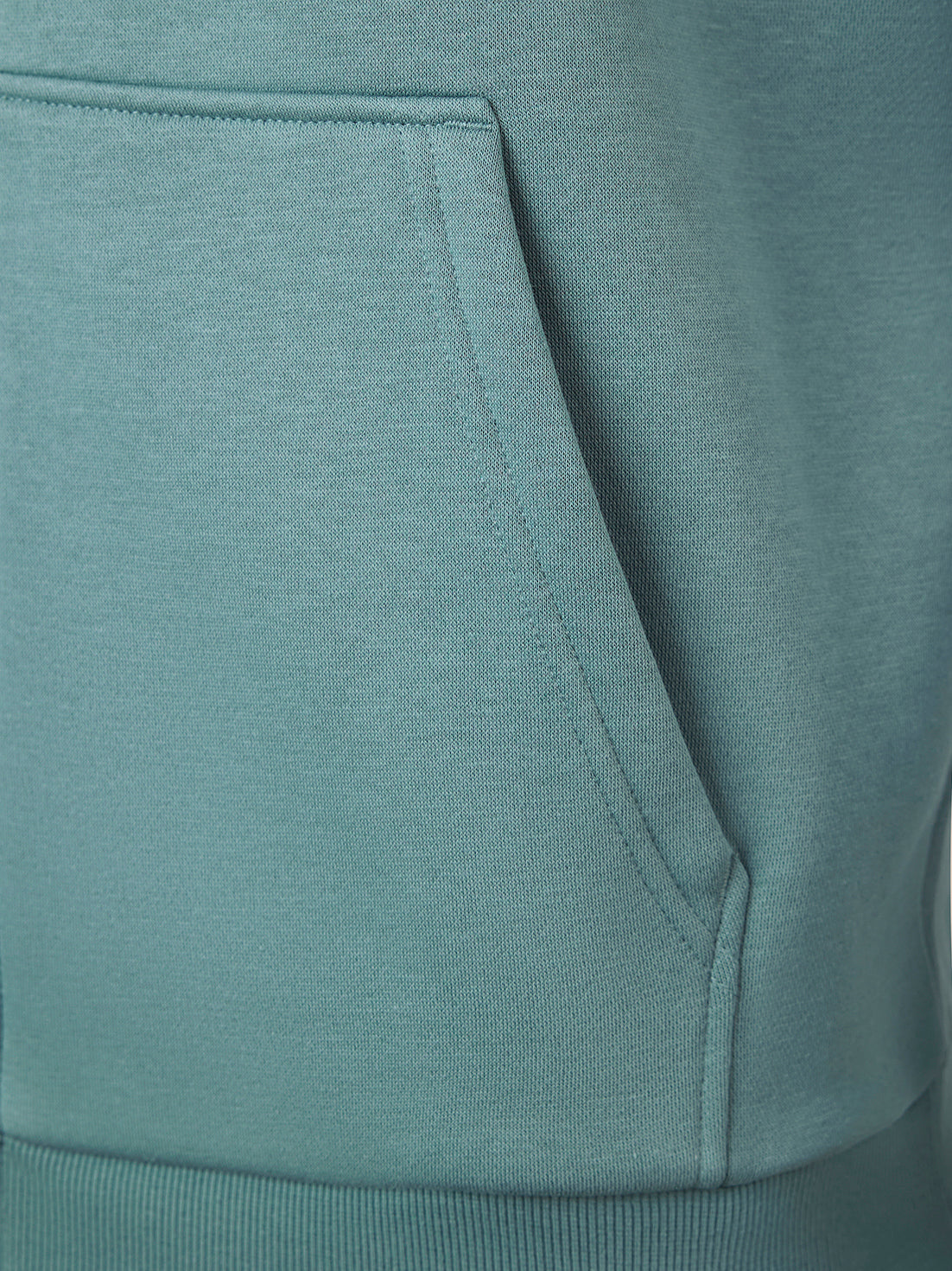 Close-up of a dusty teal-green hoodie showing the texture of the fabric and the edge of the front kangaroo pocket.