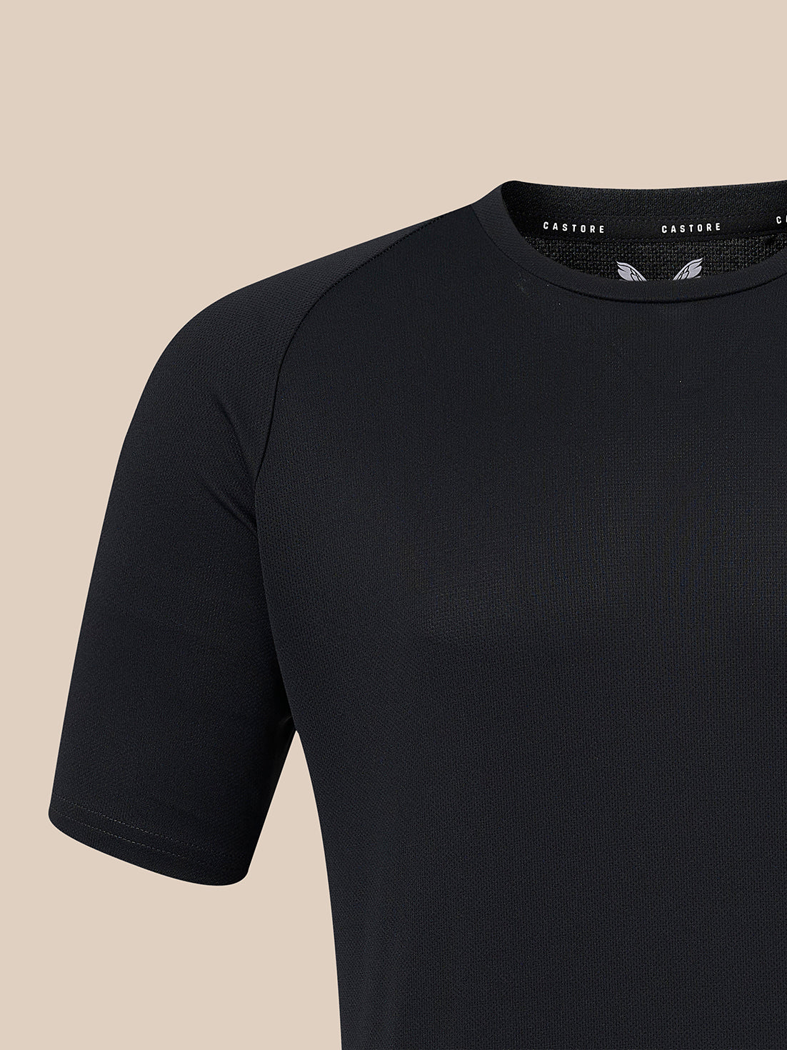 A close-up of a black short-sleeve athletic shirt with raglan sleeves, shown against a solid beige background. The brand name 'CASTORE' is visible on the inner neck label.