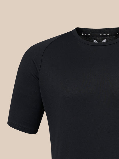 A close-up of a black short-sleeve athletic shirt with raglan sleeves, shown against a solid beige background. The brand name 'CASTORE' is visible on the inner neck label.