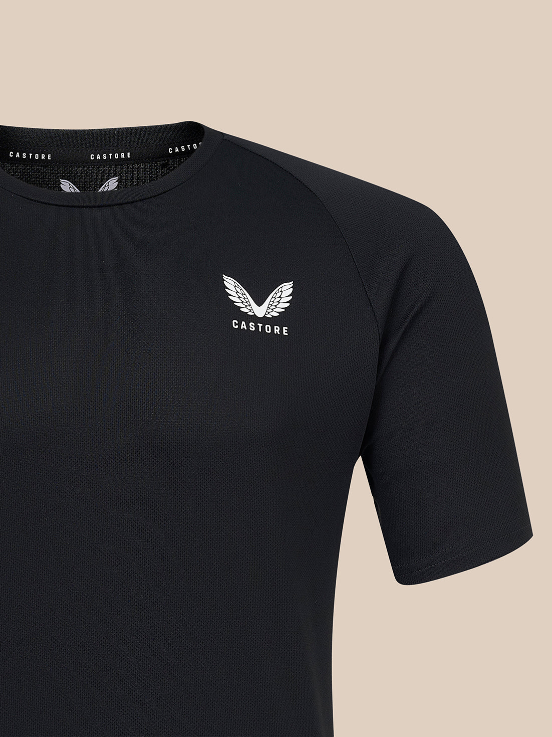 A close-up of a black short-sleeve athletic t-shirt with a white winged logo and the brand name 'CASTORE' printed on the left chest, set against a solid beige background.