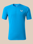 A bright blue short-sleeve athletic t-shirt with a small white winged logo and the brand name 'CASTORE' printed on the left chest, displayed on a solid beige background.