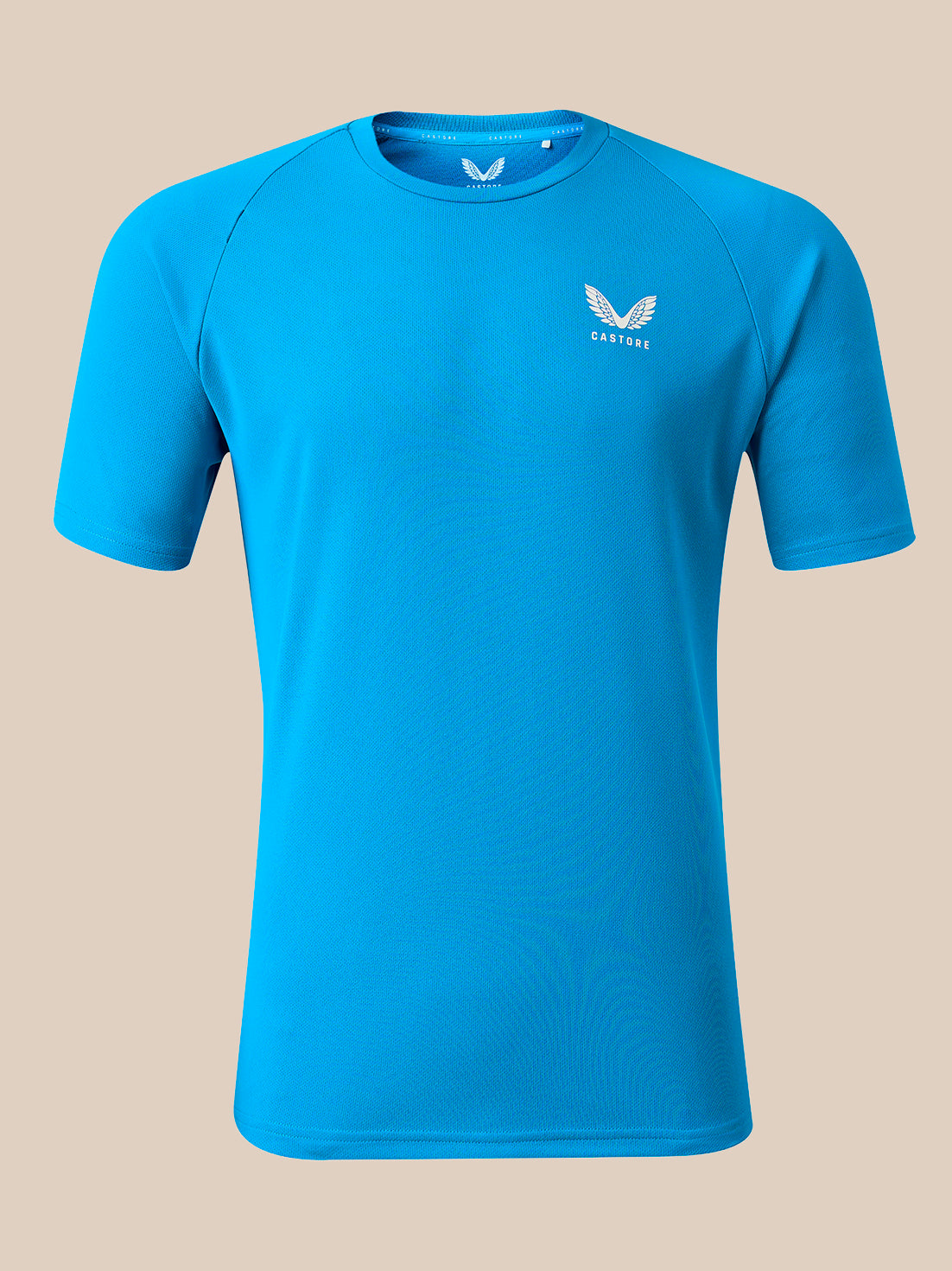 A bright blue short-sleeve athletic t-shirt with a small white winged logo and the brand name 'CASTORE' printed on the left chest, displayed on a solid beige background.