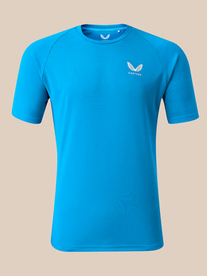 A bright blue short-sleeve athletic t-shirt with a small white winged logo and the brand name 'CASTORE' printed on the left chest, displayed on a solid beige background.