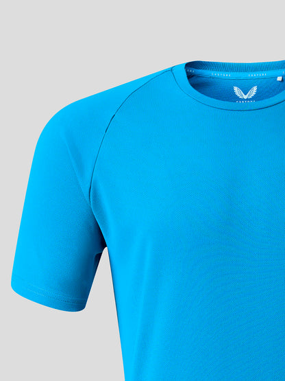 A close-up of a bright blue short-sleeve athletic t-shirt with raglan sleeves and a white wing logo on the inside of the collar, set against a solid light gray background.