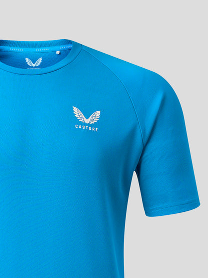 A close-up of a bright blue athletic t-shirt featuring a white winged logo and the brand name 'CASTORE' printed on the left chest, set against a solid light gray background.