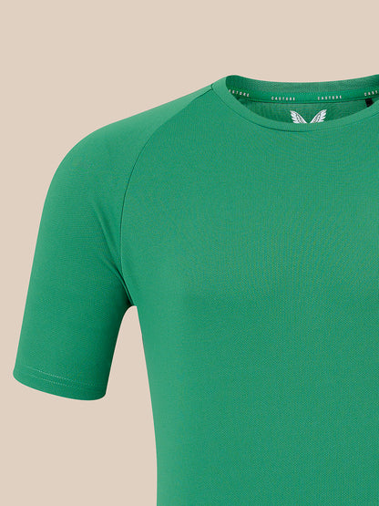 A close-up of a green short-sleeve athletic t-shirt on a solid beige background, showing the collar with a white wing logo and the brand name 'CASTORE' printed inside.