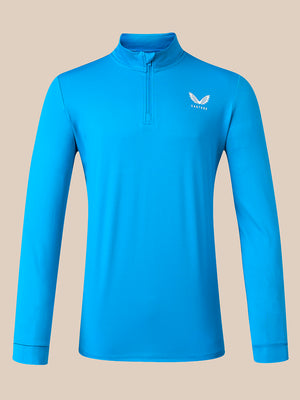A bright blue long-sleeve quarter-zip athletic pullover with a small white winged logo on the left chest, displayed on a solid beige background.