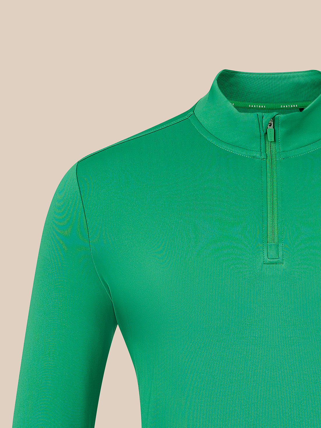 A close-up of a bright green long-sleeve quarter-zip athletic top on a model, showing the collar and zipper against a solid beige background.