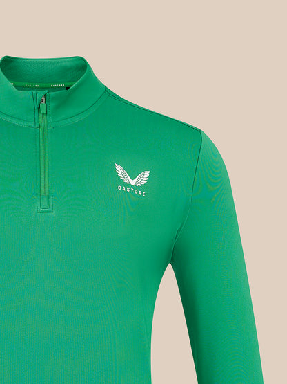 A close-up of a bright green long-sleeve quarter-zip athletic top with a white winged logo and the word 'CASTORE' on the left chest, set against a solid beige background.