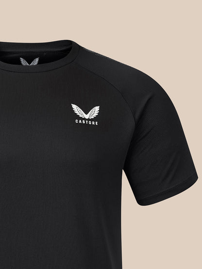 A close-up of a black short-sleeve athletic t-shirt featuring a white winged logo and the brand name 'CASTORE' on the left chest, set against a solid beige background.