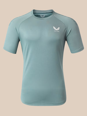 A light blue athletic short-sleeve t-shirt with a white wing logo and the brand name 'Castore' printed on the left chest, displayed on a neutral beige background.
