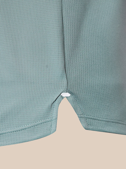 Close-up of a sage green textured mesh garment, showing the side seam and a small white elastic loop near the hem, set against a solid beige background.