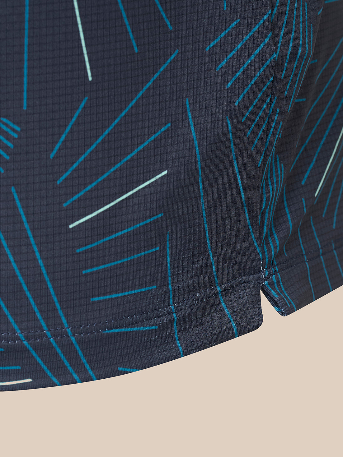 Close-up of a dark navy athletic fabric with a geometric line pattern in bright blue and white, showing the texture and hem stitching.