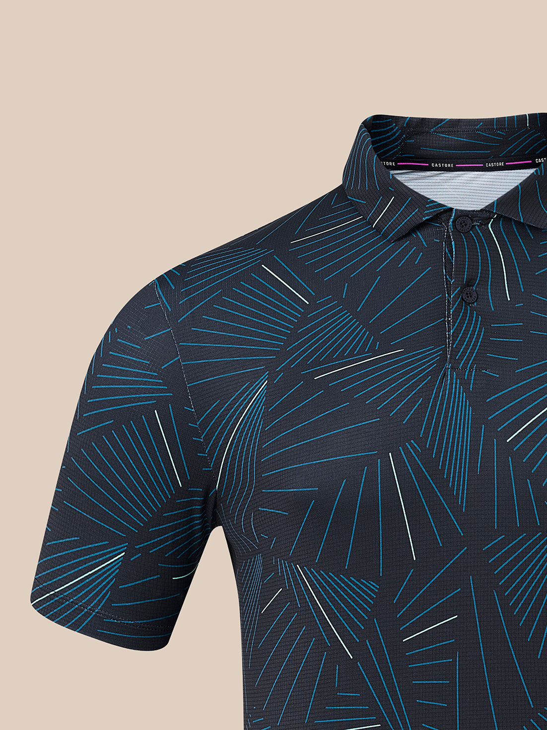Close-up of a short-sleeve polo shirt with a dark navy base and an abstract geometric line pattern in bright blue and thin white stripes, shown against a solid beige background.