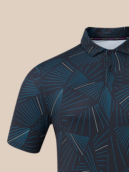 Close-up of a short-sleeve polo shirt with a dark navy base and an abstract geometric line pattern in bright blue and thin white stripes, shown against a solid beige background.