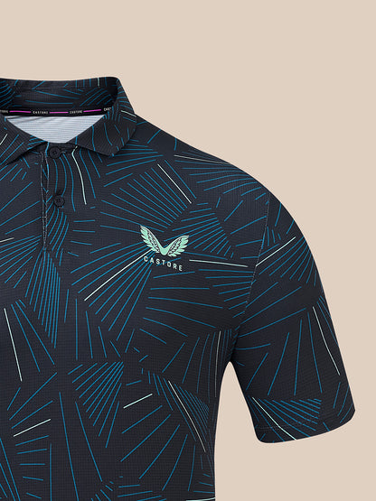 A close-up of a short-sleeve polo shirt with a dark navy base and an abstract geometric line pattern in teal, blue, and white. The chest features a teal winged logo with the text 'CASTORE.