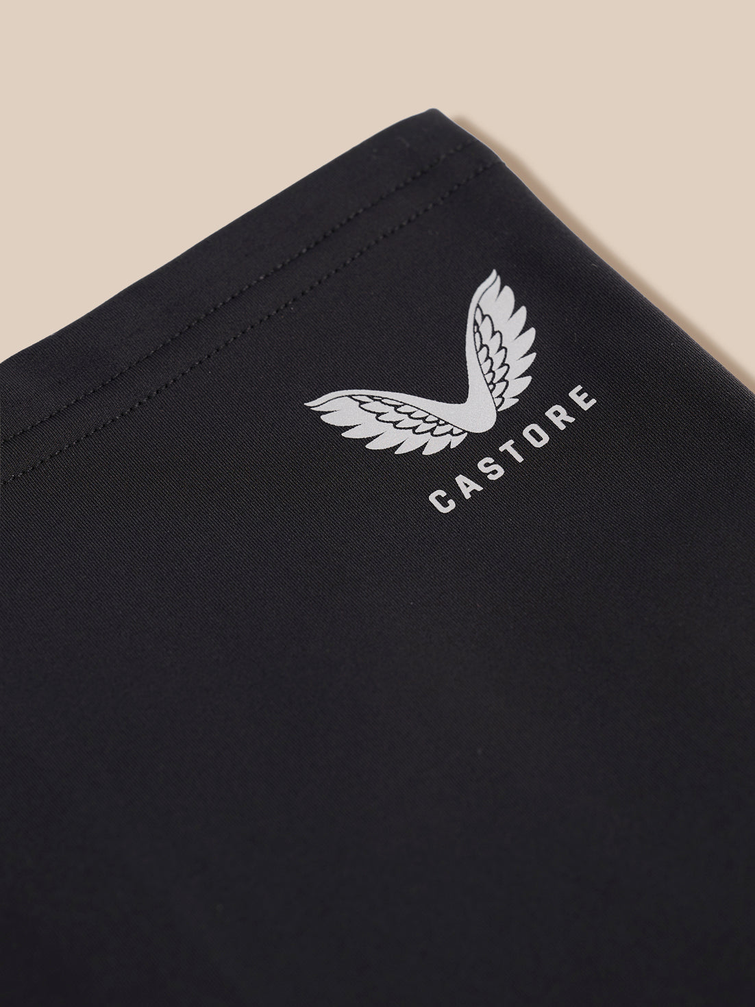 Close-up of a black garment corner with a white embroidered wing logo and the word CASTORE, shown against a light beige background.