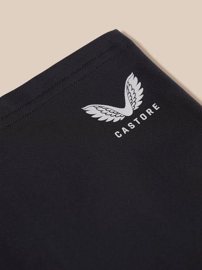 Close-up of a black garment corner with a white embroidered wing logo and the word CASTORE, shown against a light beige background.