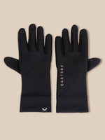 A pair of black long gloves laid flat on a light beige background. One glove shows the back with a small black logo tab near the cuff, and the other shows the front with the vertical brand name 'CASTORE' printed in white.