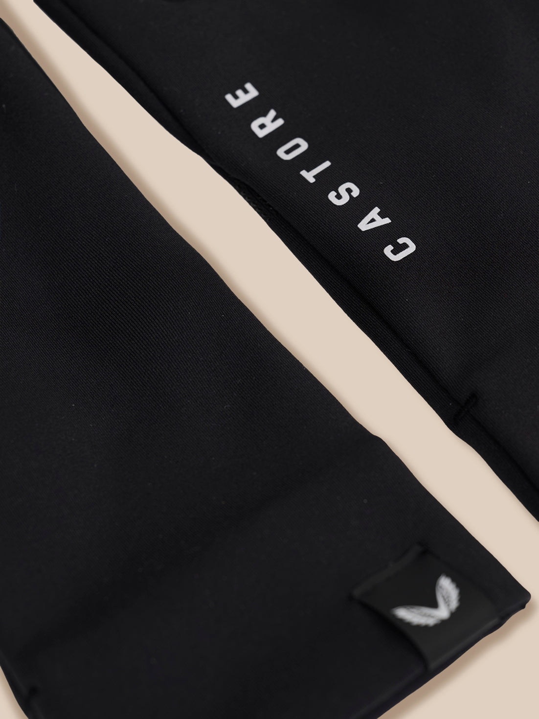 Close-up of a black garment with a diagonal beige stripe, white 'CASTORE' text, and a small white wing logo patch near the bottom.