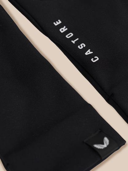 Close-up of a black garment with a diagonal beige stripe, white 'CASTORE' text, and a small white wing logo patch near the bottom.