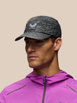 A man wearing a dark gray heathered athletic cap with a white wing logo and the brand name CASTORE' on the front, paired with a bright pink athletic jacket, set against a solid beige background.