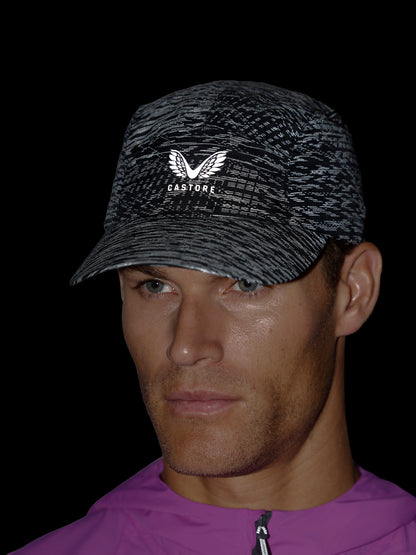 A close-up of a man wearing a black and gray patterned baseball cap with a white wing logo and the brand name 'CASTORE' on the front, set against a solid black background.