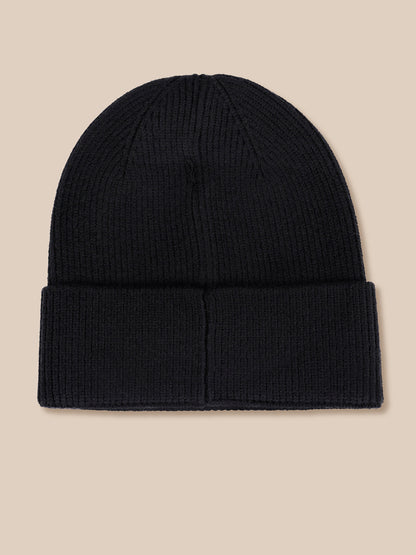 A black ribbed knit beanie hat with a folded cuff, shown flat against a solid beige background.