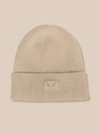 A light beige ribbed knit beanie hat with a folded cuff and a small rectangular logo patch on the front, shown against a solid beige background.