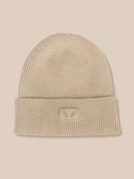 A light beige ribbed knit beanie hat with a folded cuff and a small rectangular logo patch on the front, shown against a solid beige background.