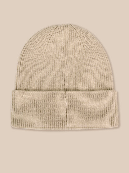 A light beige ribbed knit beanie hat with a folded cuff, shown against a solid light beige background.