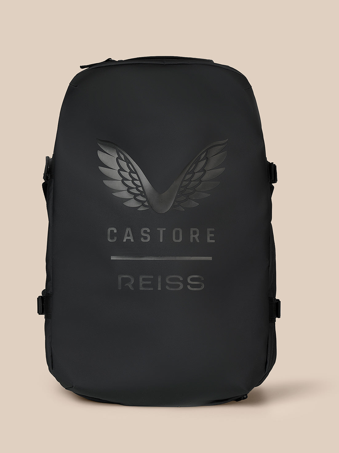 A black Castore Reiss backpack with a tonal dark gray wing logo and brand name printed on the front, set against a solid beige background.