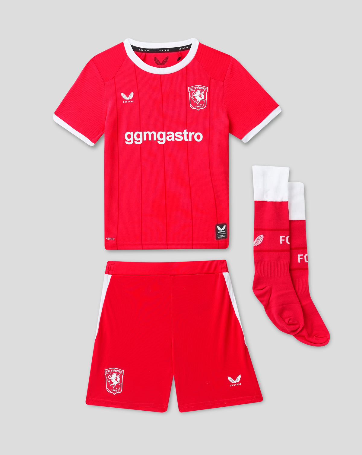 Front view of red FC Twente junior home kit with white collar and club crest on the chest, paired with matching socks.
