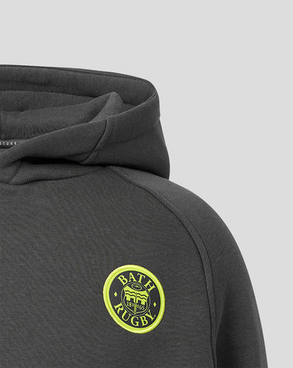 Close-up of a dark gray hooded sweatshirt showing the shoulder and chest area with a circular yellow and green 'Bath Rugby' crest patch on the left chest, set against a light gray background.