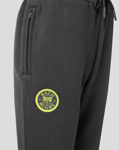 Close-up of dark gray sweatpants with a yellow circular Bath Rugby logo patch on the left thigh and a zippered pocket on the right side.