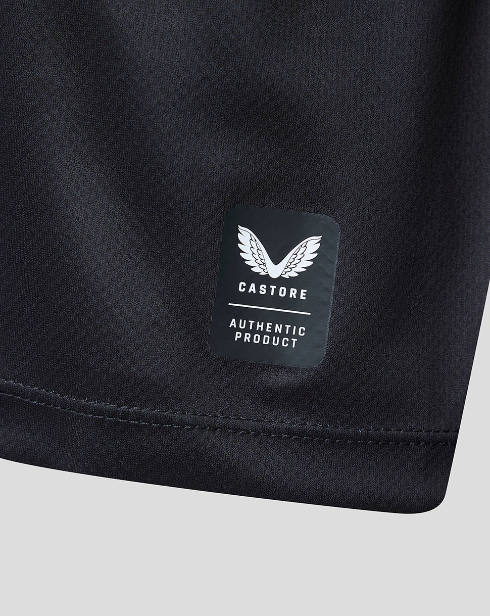 Close-up of a black athletic garment showing a sewn-on Castore Authentic Product label on the fabric, with a light gray background.
