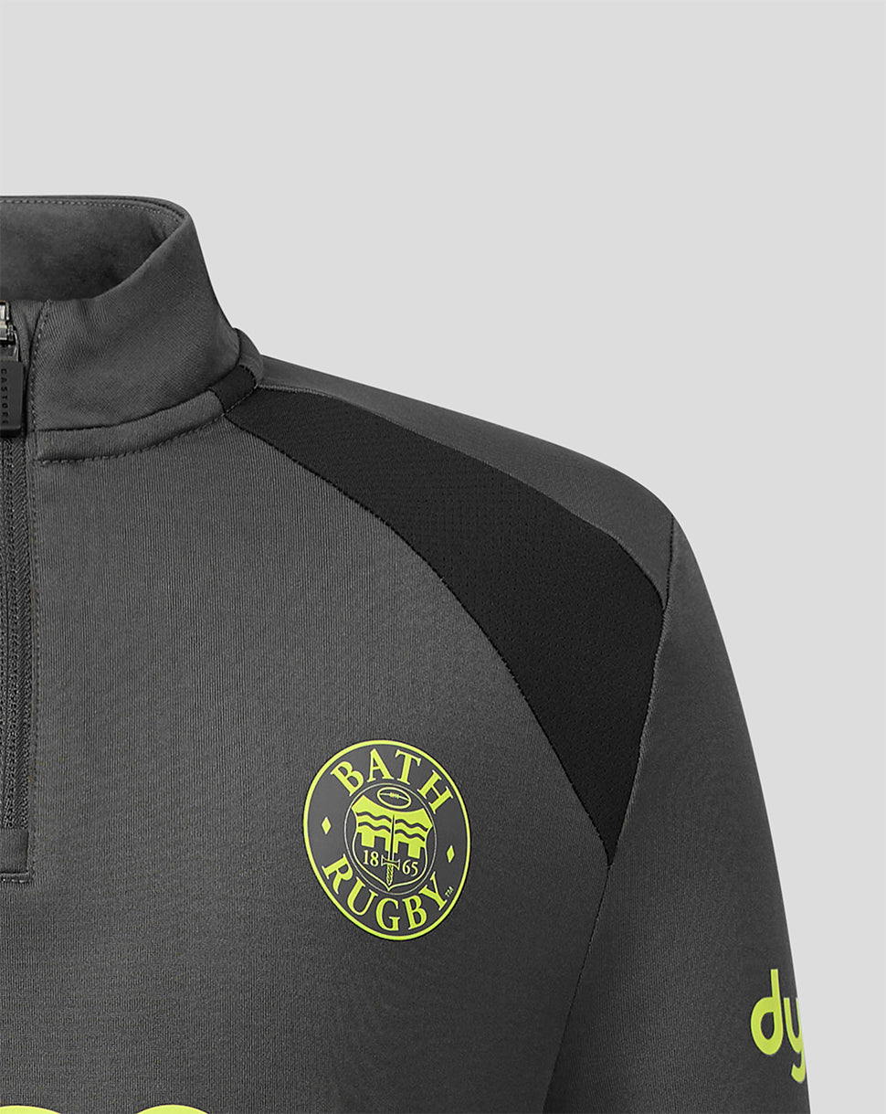 Close-up of a dark gray athletic quarter-zip pullover with a black shoulder panel, featuring a yellow circular Bath Rugby crest on the chest and a yellow logo on the sleeve, set against a light gray background.
