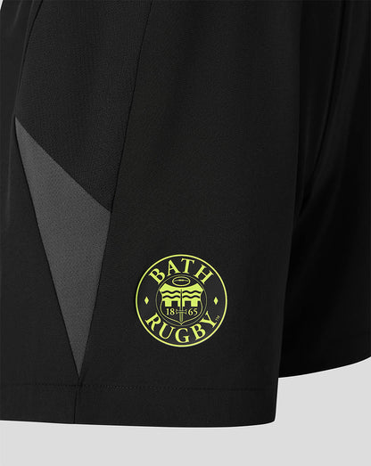 Close-up of black athletic shorts with a dark gray side panel and a circular yellow-green Bath Rugby crest on the lower left leg.