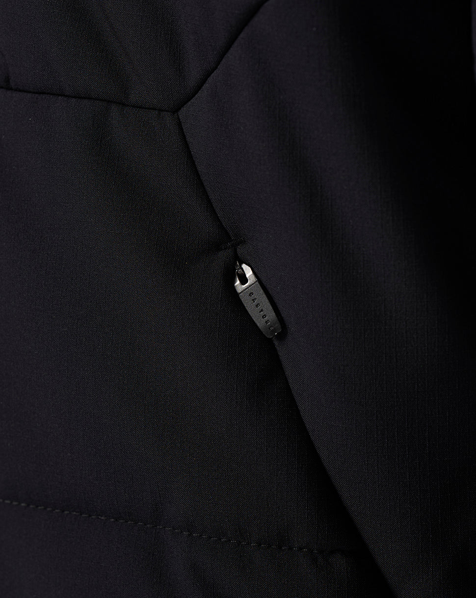 Close-up of a black quilted jacket showing a side pocket with a black zipper pull and fine fabric texture.