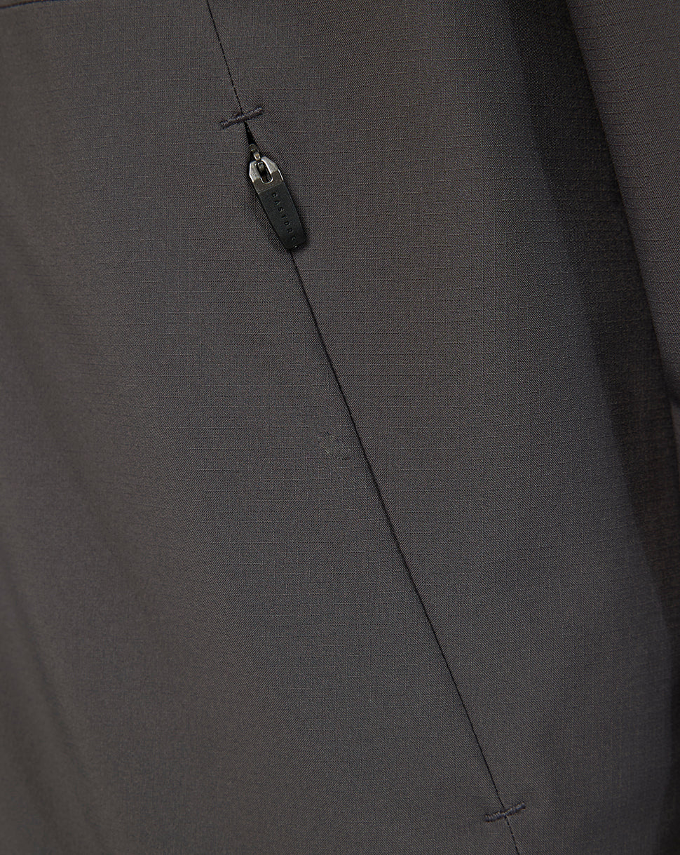 Close-up of a dark gray fabric garment showing a vertical seam, a small stitched detail, and a dark zipper pull.
