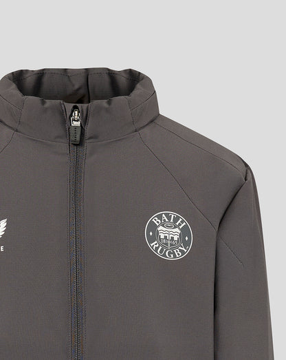 Close-up of a dark gray athletic zip-up jacket with a high collar, featuring a white circular Bath Rugby crest on the left chest and a partial white wing logo on the right chest, set against a light gray background.