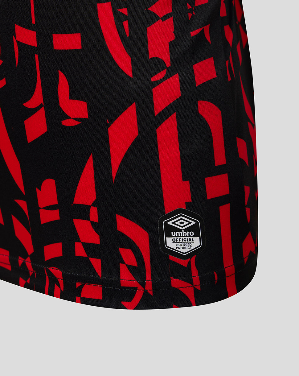 Close-up of black athletic shorts with a bold red abstract geometric pattern and a visible Umbro logo patch near the hem, shown on a light gray background.