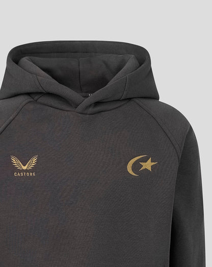 A close-up of a dark gray hooded sweatshirt featuring a gold Castore wing logo on the left chest and a gold crescent and star logo on the right chest, set against a light gray background.