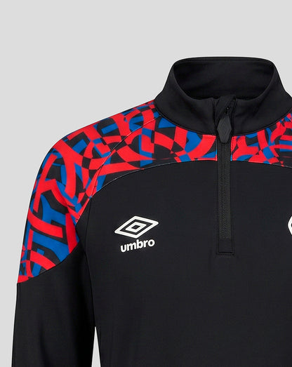 A close-up of a black athletic quarter-zip pullover with a red and blue geometric pattern on the shoulders and upper sleeves, featuring a white Umbro logo on the chest.