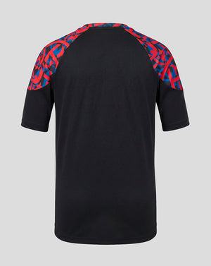 A black short-sleeve raglan t-shirt shown from the back, featuring a vibrant red and blue geometric pattern on the shoulders, set against a solid light gray background.