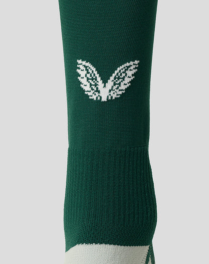A close-up of a dark green athletic sock featuring a white knit wing logo on the side and a white toe section, set against a solid light gray background.