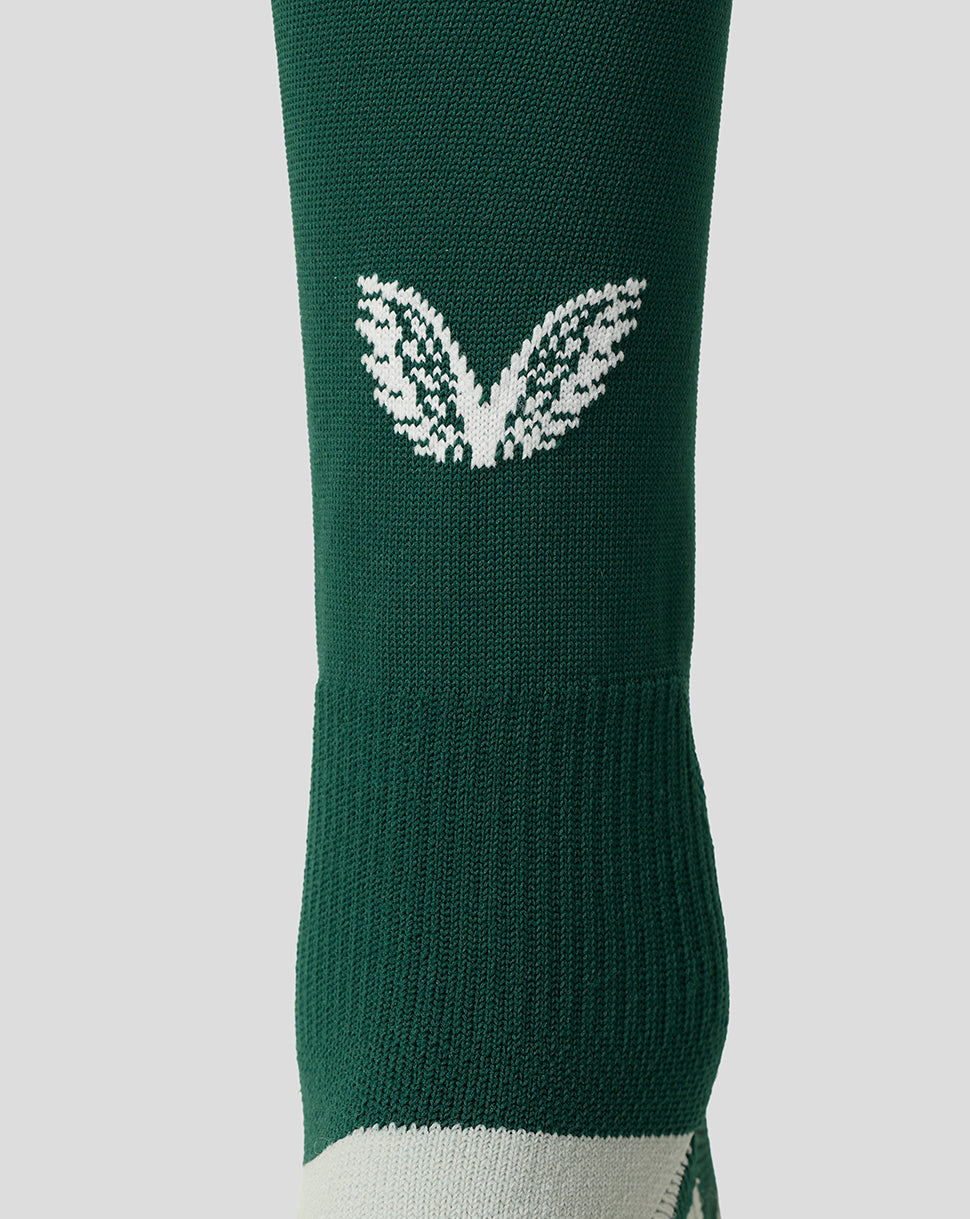 A close-up of a dark green athletic sock featuring a white knit wing logo on the side and a white toe section, set against a solid light gray background.