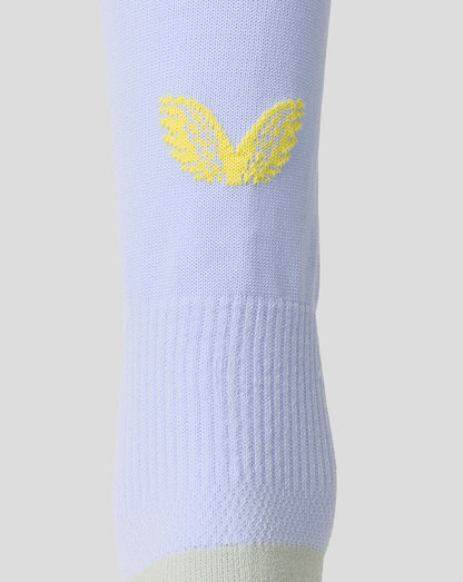 A close-up of a light periwinkle blue knit sock featuring a yellow embroidered wing logo on the upper calf, set against a solid light gray background.