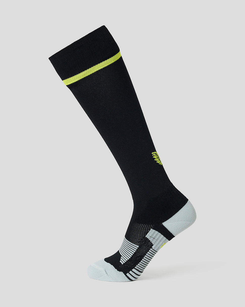 A single knee-high athletic sock in black with a bright neon yellow-green accent band near the cuff, a small matching accent on the side, and a light gray toe and heel, shown on a plain light gray background.